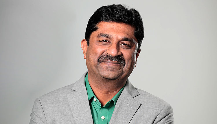 Man in a grey suit and green shirt smiling
